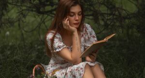 a fair-skinned white woman reading a book near trees