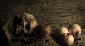 a skull, apples, and candies arranged on a mat in sepia tones