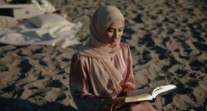 fair-skinned woman in hijab reading on the beach