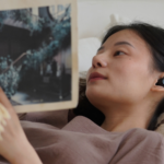 an Asian woman listening to earbuds while reading a book