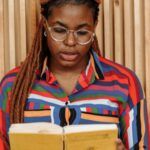 a brown-skinned Black woman with braids reading