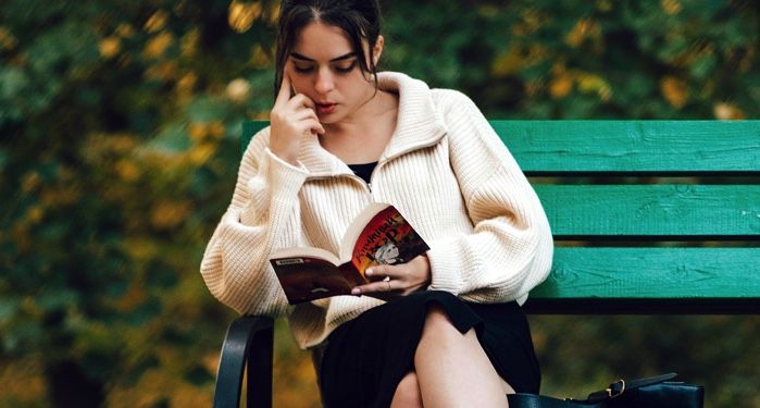 fair-skinend woman reading a book on a green park bench