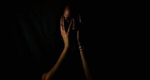 a dark photo of a brown-skinned woman obscuring her face with her hands