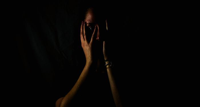 a dark photo of a brown-skinned woman obscuring her face with her hands