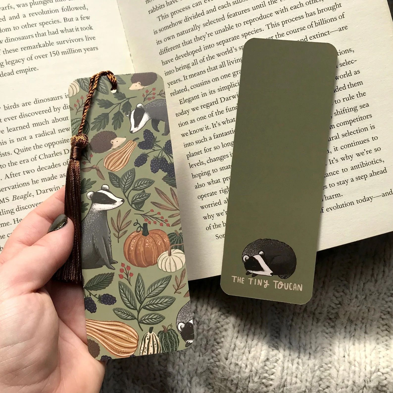 a photo of an adorable green bookmark with illustrations of badgers and hedgehogs. It has lots of fall vibes.