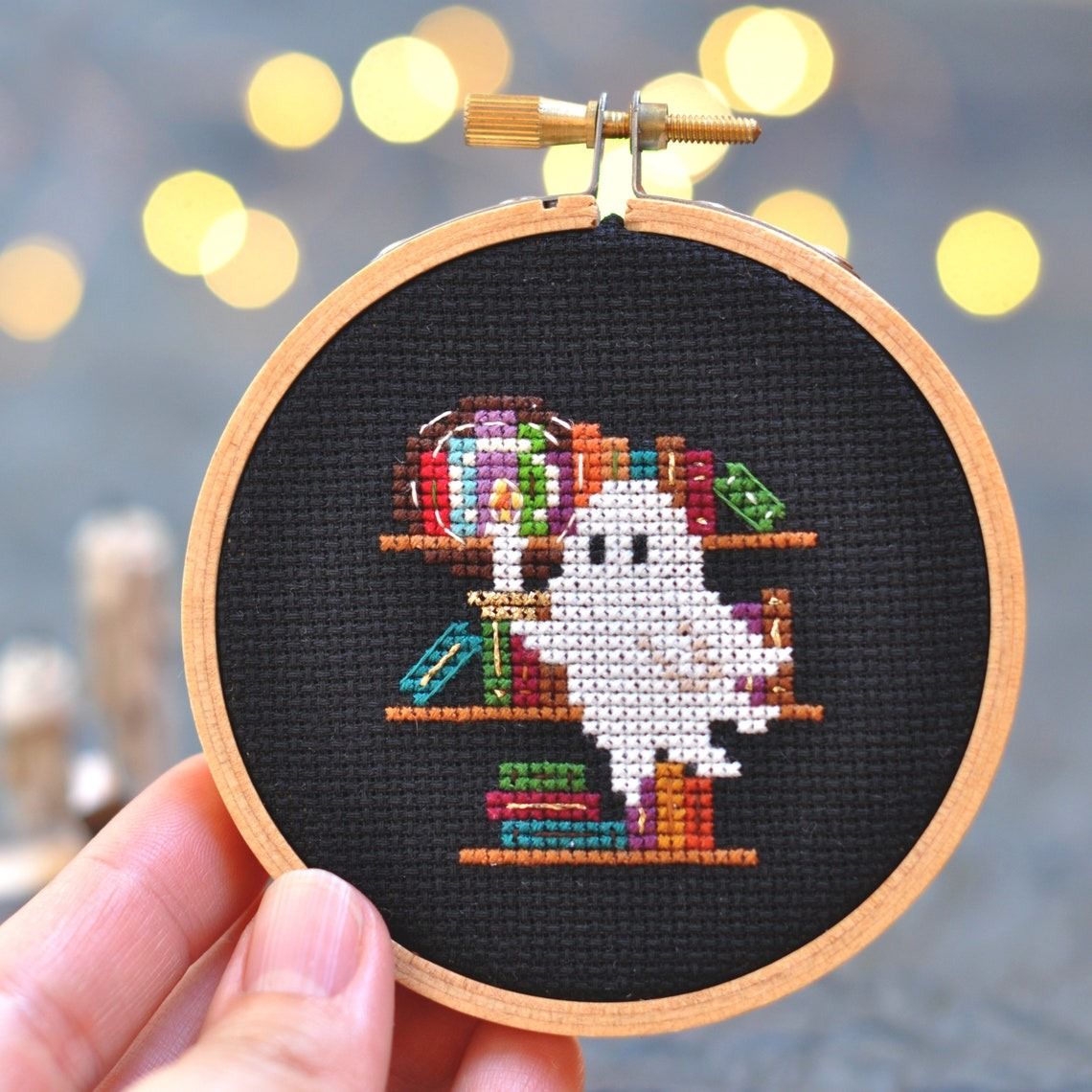 a cross stitch of a ghost holding a candle in front of bookshelves